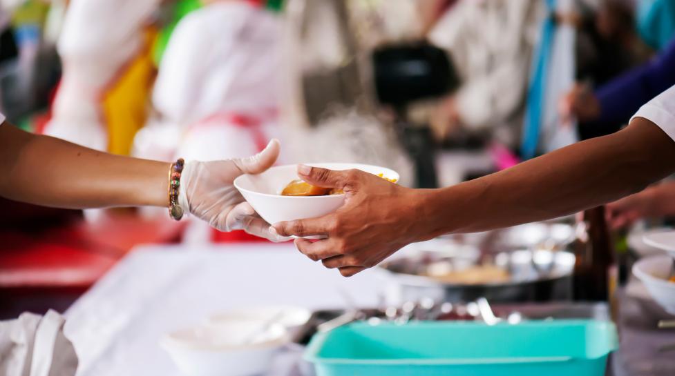 Volunteer wearing a plastic glove passing a bowl of food to someone. Only hands and arms are visible.