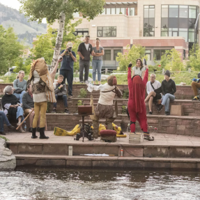 Performers dressed in costume acting for an audience next to the Boulder Creek